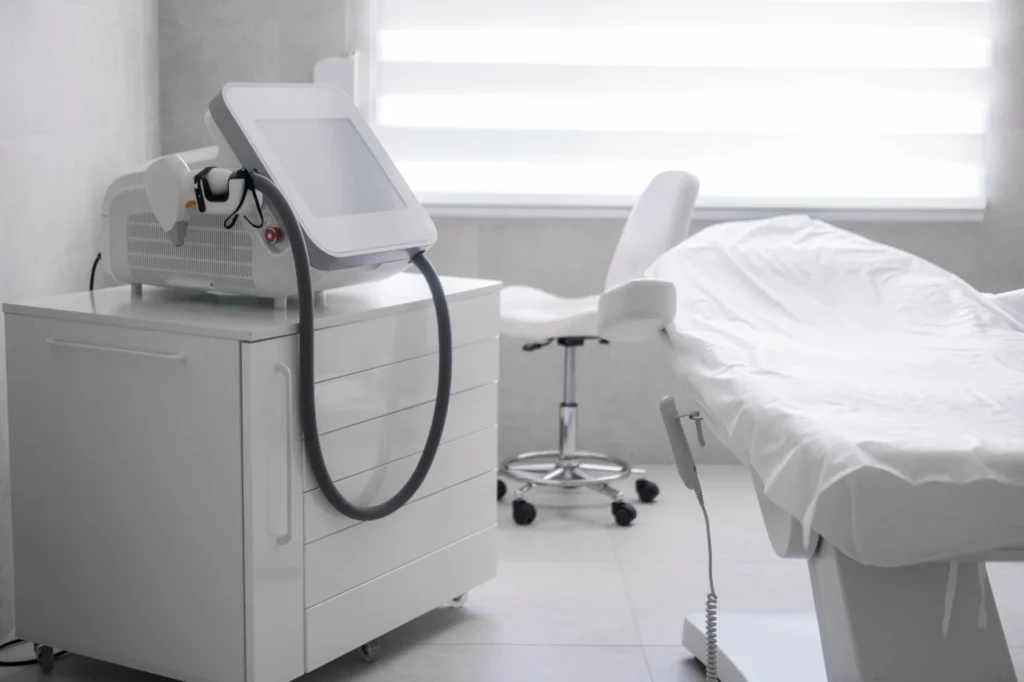 Sala de tratamiento médico con camilla blanca y dispositivo estético avanzado.